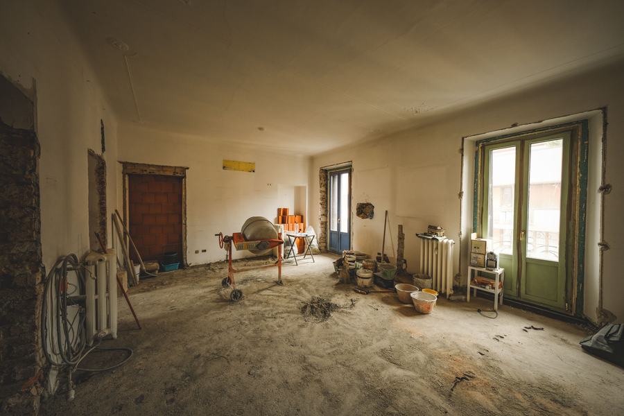 Pièce en rénovation avec portes-fenêtres vertes, bétonnière et matériaux au sol